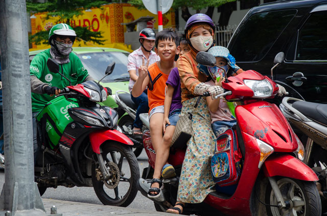 Three Vietnamese kids and his mom, are sitting on motorbike. 