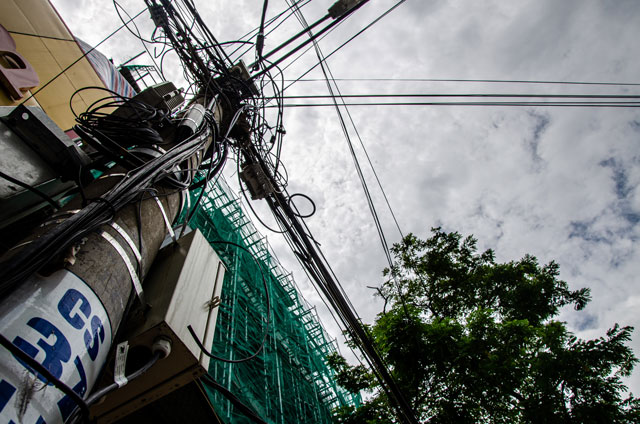 Sloup elektrického vedení obtočen kabely, za nímž se vypíná budova ve výstavbě. Výjev z města Danang.